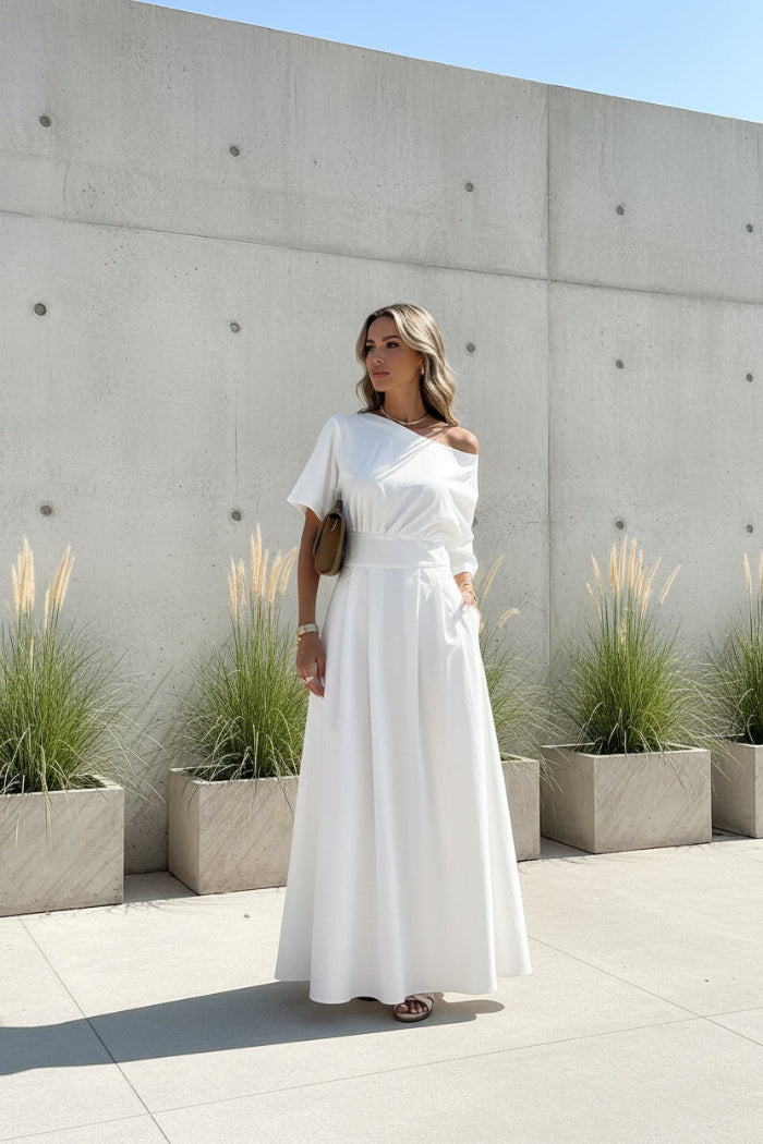 Woman wearing a white off-shoulder dress standing outdoors.