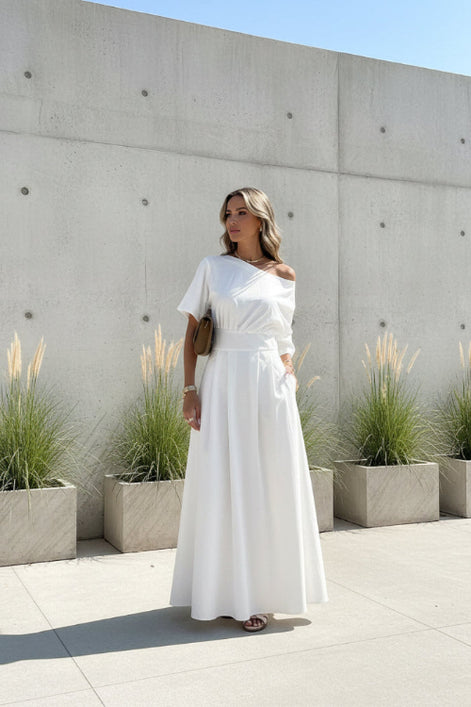Woman wearing a white off-shoulder dress standing outdoors.