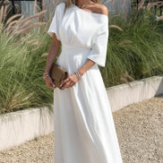 Woman in a white off-shoulder dress standing in front of tall grasses.