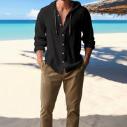 Man wearing a black hooded shirt with a beach in the background