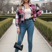 Person wearing a pink and black plaid shirt with blue jeans indoors.