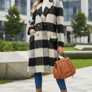 Woman wearing a black and white checkered coat with a brown bag and boots on a plain background