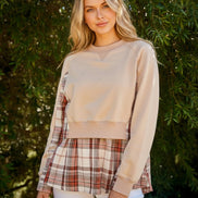 Woman wearing a beige sweater over a plaid shirt with a green outdoor background