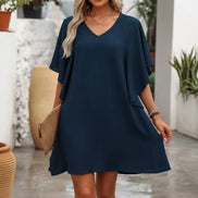 Woman wearing a navy blue dress holding a woven bag outdoors.