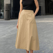 Woman wearing a black sleeveless top and beige skirt on a stone pavement.