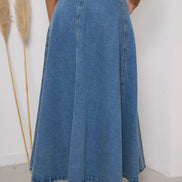 Person wearing a long blue denim skirt with a white background