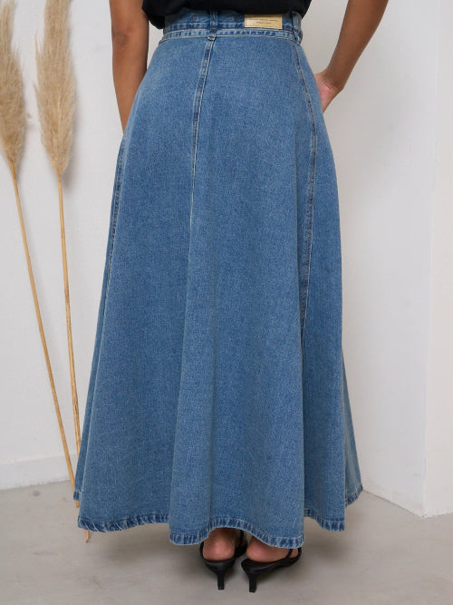 Person wearing a long blue denim skirt with a white background