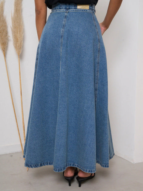 Person wearing a long blue denim skirt with a white background