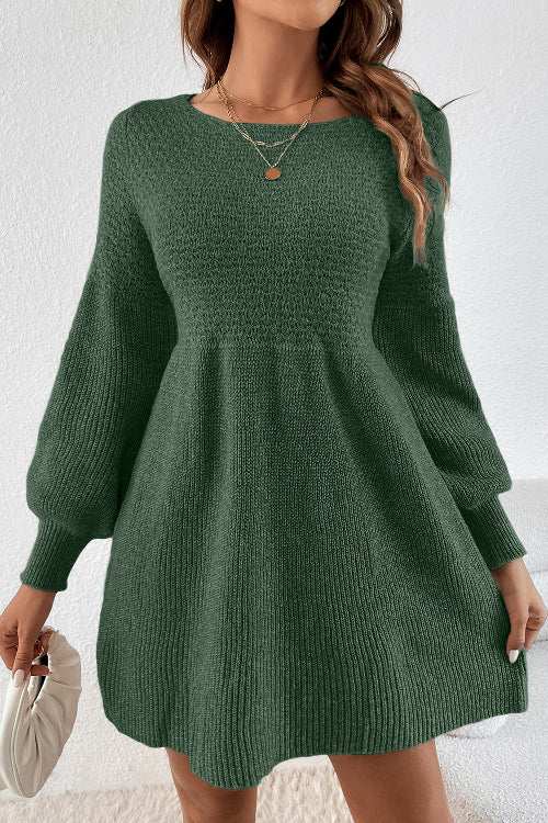 A woman wearing a dark green ribbed knit mini dress with balloon sleeves, holding a white clutch purse against a textured white wall.