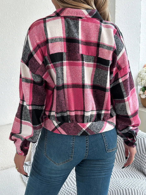 Person wearing a pink and black plaid shirt with blue jeans indoors.