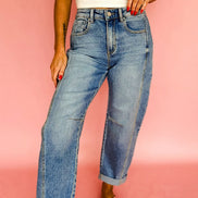 A person wearing light-wash blue straight-leg jeans with rolled cuffs, paired with a white ribbed tank top