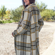Woman wearing a plaid coat outdoors with trees and clear sky in the background