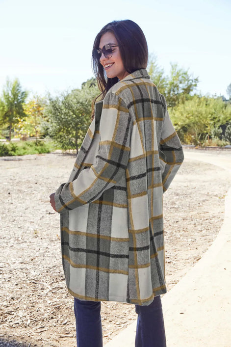 Woman wearing a plaid coat outdoors with trees and clear sky in the background