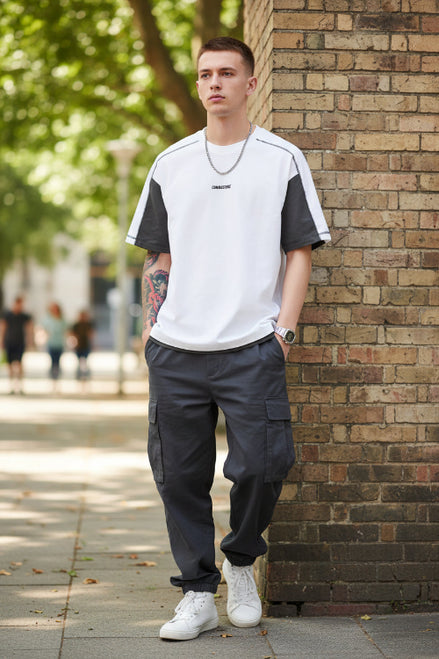 Man leaning against a brick wall wearing a white and black shirt with gray pants.