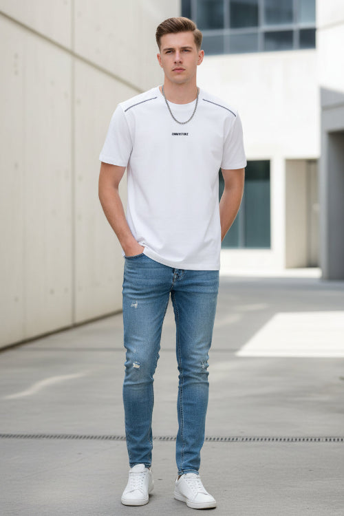 Man wearing a white t-shirt and blue jeans standing outdoors.