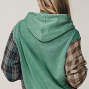 A person shown from the back wearing a hooded sweatshirt with a washed green body and contrasting plaid sleeves i