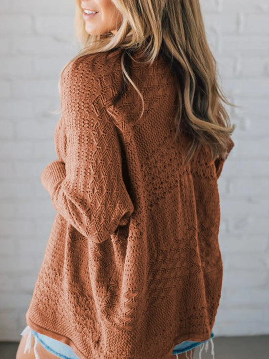 Person wearing a brown cable knit sweater against a white brick wall.
