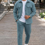 A man wearing a matching dusty blue two-piece tracksuit with a button-up shirt jacket and matching jogger pants, 