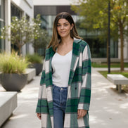 Woman wearing a green and white plaid coat over a white shirt and blue jeans against a plain background