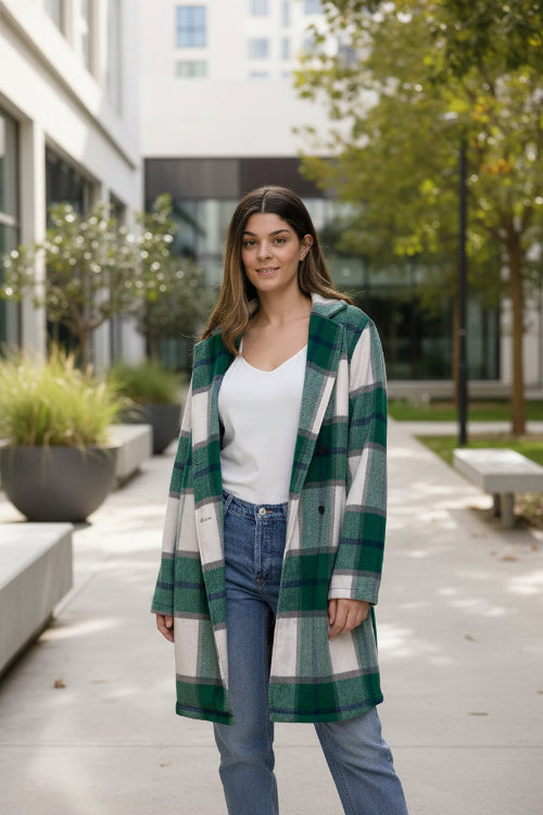 Woman wearing a green and white plaid coat over a white shirt and blue jeans against a plain background