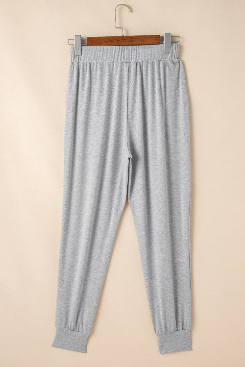 Gray sweatpants hanging on a wooden hanger against a beige background