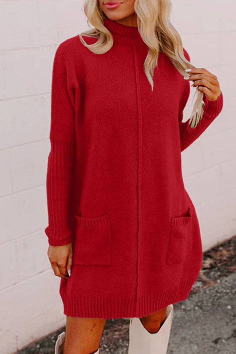 Red sweater dress worn by a person against a white brick wall.