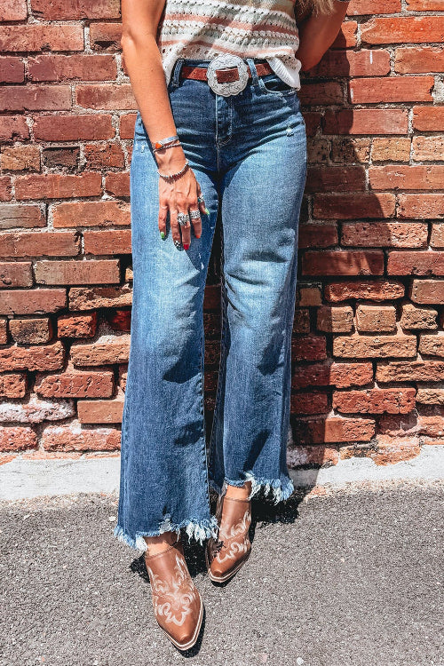 Person wearing blue jeans and brown boots against a brick wall.