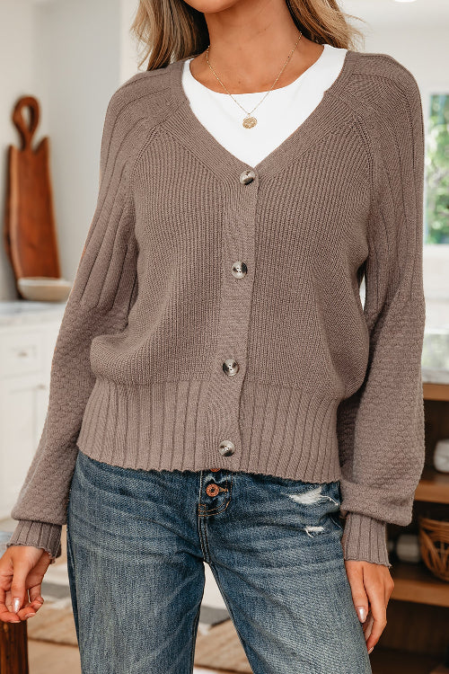 Person wearing a brown button-up sweater over a white shirt with blue jeans indoors.