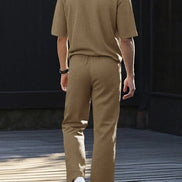 A man viewed from behind wearing a matching tan short-sleeve knit polo shirt and trousers set, 