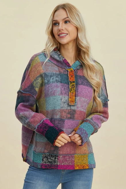 A woman modeling a multicolor patchwork plaid pullover hoodie with a hood, kangaroo pocket, and ribbed cuffs, 