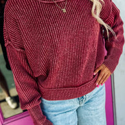 A woman wearing a ribbed knit crewneck sweater in a deep burgundy red, paired with light blue jeans and a gold necklace, 