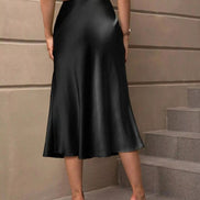 Person wearing a black satin skirt standing on steps with a neutral wall background