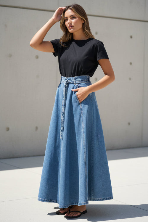 Person wearing a black t-shirt and blue denim skirt against a white wall.