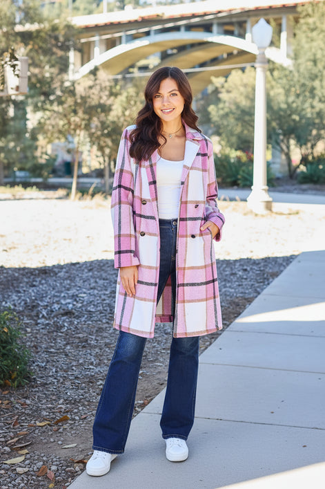 A woman wearing a pink, white, and black plaid double-breasted coat over a white tank top and dark blue jeans, 
