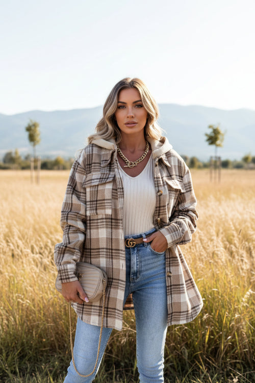 Person wearing a plaid jacket over a white top and blue jeans, holding a beige handbag against a gray background.