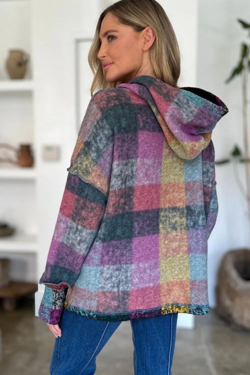 Woman wearing a multicolored checkered hoodie in a room with white walls and a plant.