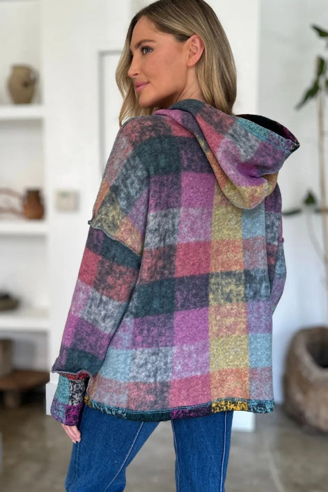 Woman wearing a multicolored checkered hoodie in a room with white walls and a plant.