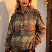 A woman wearing a distressed, multi-colored plaid pullover hoodie with a front button placket and drawstring hood, 