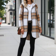 Person wearing a plaid coat holding a coffee cup against a textured wall.