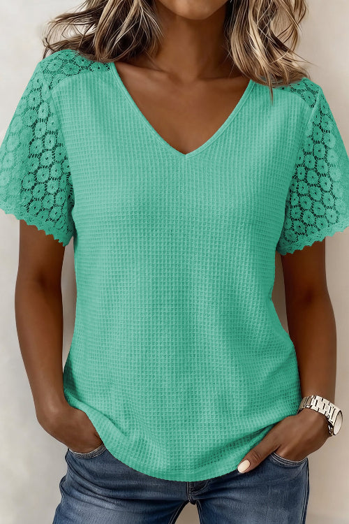 A woman wearing a mint green waffle-knit short-sleeve top with floral lace shoulder panels and a V-neckline, paired with blue jeans.
