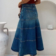 Person wearing a long blue denim skirt with a white background