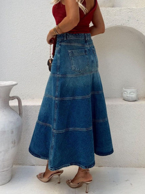 Person wearing a long blue denim skirt with a white background