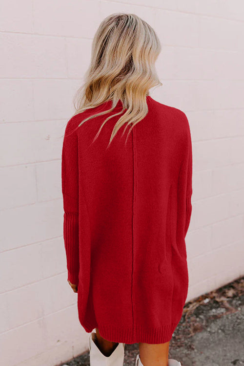 Person wearing a red sweater dress against a white brick wall.