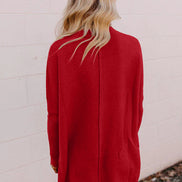 Person wearing a red sweater dress against a white brick wall.