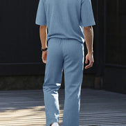 A man viewed from behind wearing a light blue knit matching set consisting of a short-sleeve polo shirt and wide-leg trousers, 