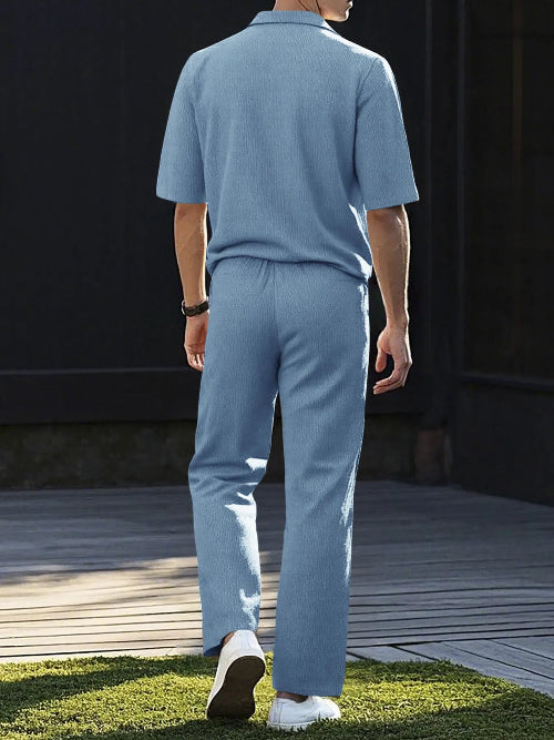 A man viewed from behind wearing a light blue knit matching set consisting of a short-sleeve polo shirt and wide-leg trousers, 