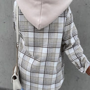 Person wearing a plaid coat with a hood against a gray wall
