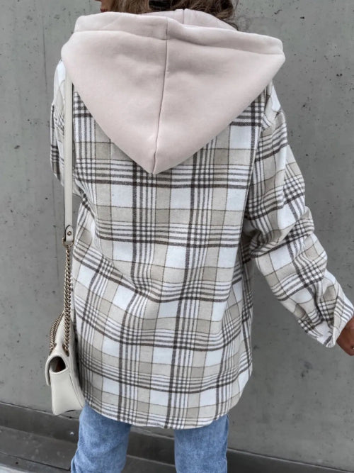 Person wearing a plaid coat with a hood against a gray wall