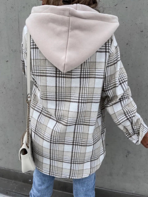 Person wearing a plaid coat with a hood against a gray wall
