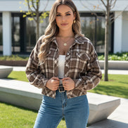 Woman wearing a plaid shirt and jeans holding a phone and black handbag.